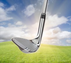 Chrome golf club wedge iron against grass and blue sky background