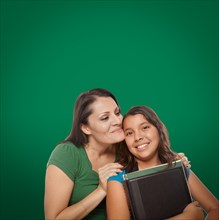 Blank chalk board behind proud hispanic mother and daughter student
