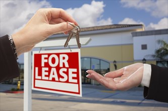 Real estate agent handing over the keys in front of vacant business office and for lease sign