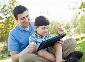 Happy father and son playing on a computer tablet outside