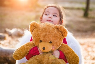 Cute young mixed-race baby girl hugging teddy bear outdoors