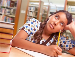 Daydreaming hispanic girl student with pencil and books studying in library