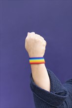 Detail of arm and hand of woman wearing gay wristband on purple background