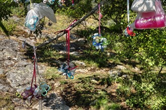 Many discarded dummies and colourful teat bottles in plastic bags hang on a tree