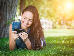 Attractive happy mixed-race young female laying in the grass texting on her cell phone outside