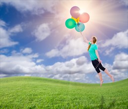 Young girl being carried up and away by balloons that she is holding above the grass field below