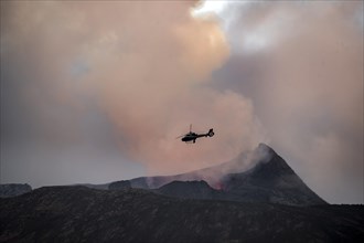 Helicopter flying over smoking active volcanic crater