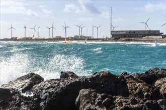 Water splashing on the rocks with windsurfers and windmills in the background
