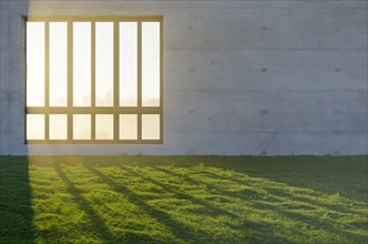 Window with bright sun light shining through concrete wall in grass and rocks field