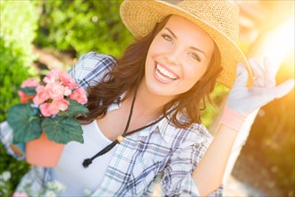 Happy young adult woman wearing hat and gloves gardening outdoors