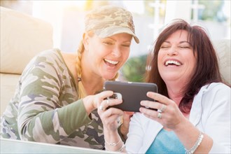 Two female friends laugh while using A smart phone on the patio