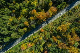 View from above of a diagonally running road with moving cars in an autumnal landscape