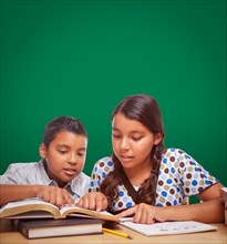Blank chalk board behind hispanic boy and girl having fun studying together