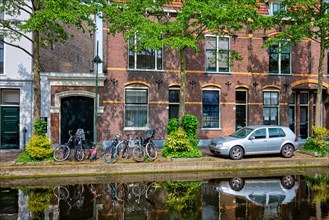 Cars and bicycles parked along the canal in street of Delft with reflection. Delft