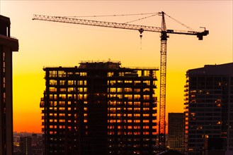 Silhouette of crane and building under construction at dusk