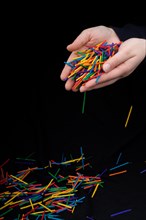 Hand letting coloured wooden sticks fall on black background