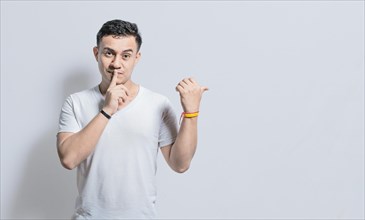 Handsome man with finger on lip pointing to the side on isolated background