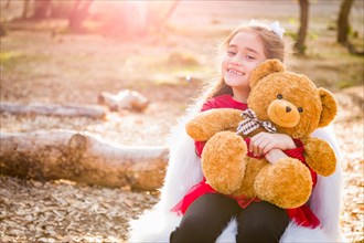 Cute young mixed-race girl hugging teddy bear outdoors