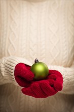 Woman wearing seasonal red mittens holding green christmas ornament