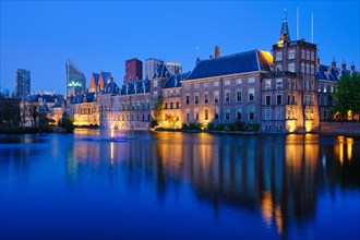 View of the Binnenhof House of Parliament and the Hofvijver lake with downtown skyscrapers in background illuminated in the evening. The Hague