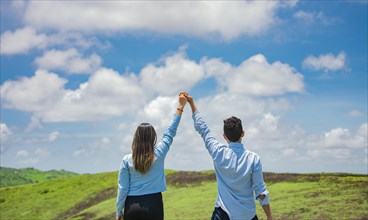 Back view of couple on the hill with hands raised to the sky