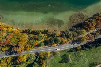 View from above of a moving car on a road next to a lakeshore in autumn