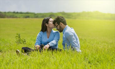 Romantic couple sitting on the grass kissing their foreheads