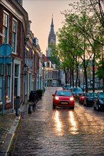 Delft cobblestone street with car in the rain with Nieuwe Kerk church tower in background. Delft