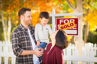 Young mixed-race chinese and caucasian family in front of sold for sale real estate sign and fall yard