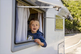 Happy small boy looking through the RV's window parked along the road