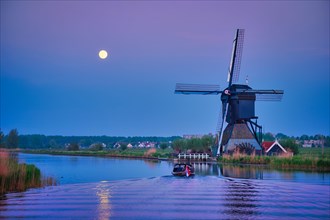 Netherlands rural landscape with windmills at famous tourist site Kinderdijk in Holland in twilight with full moon and boat in canal