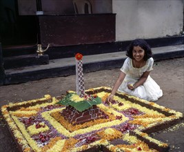 A girl doing floral decoration or pookalam during Onam festival in Kodungallur