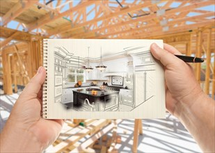 Male hands holding pen and pad of paper with custom kitchen illustration inside construction framing