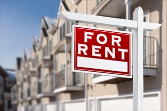 For rent real estate sign in front of a row of apartment condominiums balconies and garage doors
