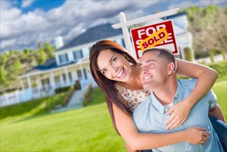 Playful excited military couple in front of home with sold real estate sign