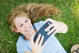 Young adult woman laying in grass taking a selfie with her smart phone