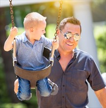 Happy young boy having fun on the swings with his father at the playground