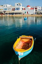 Blue fishing boat in port harbor of Chora town on Mykonos island with orthodox church in background
