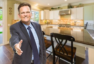 Smiling male agent reaching for hand shake in beautiful new kitchen
