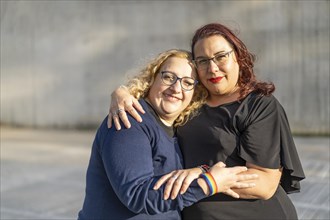 Couple of lesbian women hugging in a park looking at the camera