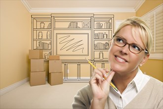 Daydreaming woman holding pencil in empty rom with built in shelf design drawing on wall