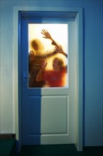 Gruselige Silhouette von zwei jungen Erwachsenen im Gegenlicht hinter einer verschlossenen Glastuere