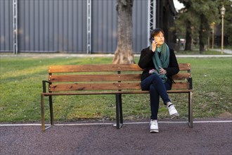 Latin woman sitting on a bench in a park talking on a cell phone