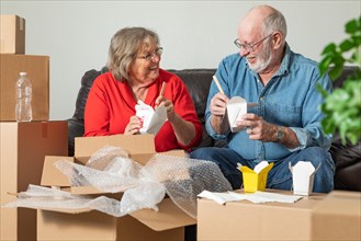 Senior couple enjoying chinese food surrounded by moving boxes