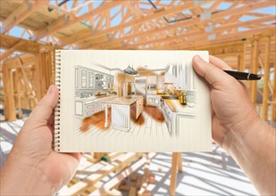 Male hands holding pen and pad of paper with custom kitchen illustration inside construction framing