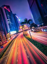 Street traffic in Hong Kong at night. Office skyscraper buildings and busy traffic on highway road with blurred cars light trails. Hong Kong