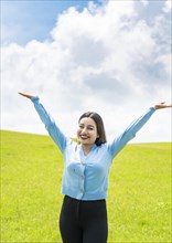 Smiling young woman spreading her arms in the field
