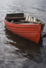 Leeres rote Ruderboot am Seeufer bei Regenwetter
