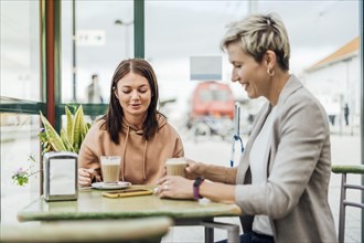 Two female friends drinking coffee and enjoying time in the cafe at railway station