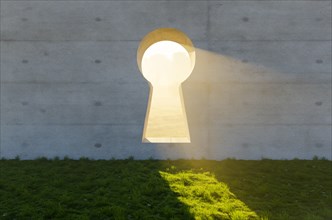 Bright sun light shining through keyhole in concrete wall in grass and rocks field
